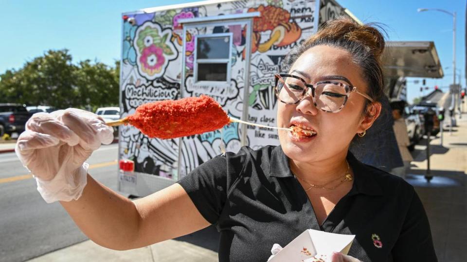 Teresa Choi of the Mochilicious Society food trailer takes a bite of a Nothin’ but Mozzy Cheese Korean corndog outside the trailer during their grand opening next to The Grand in downtown Fresno on Tuesday, Sept. 5, 2023.