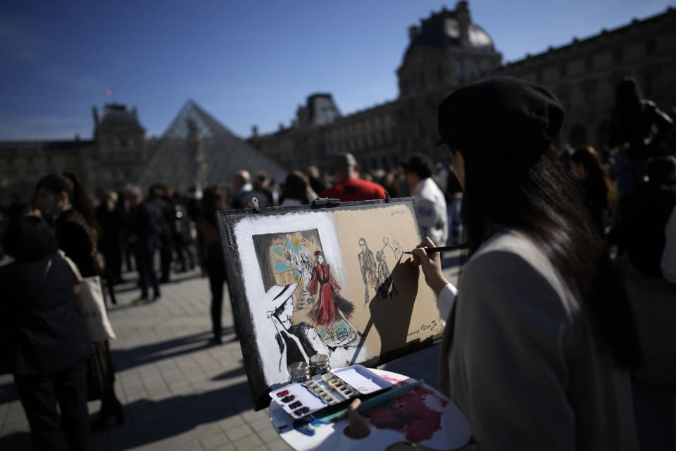 An artist paints fashion lovers in the courtyard of the Louvre museum during Louis Vuitton ready-to-wear Spring/Summer 2023 fashion collection presented Tuesday, Oct. 4, 2022 in Paris. (AP Photo/Christophe Ena)