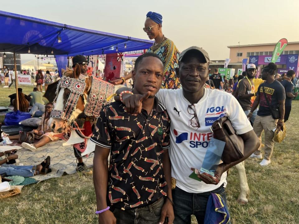 Horse Jockey duo Jonathan Lawal and his son Ebenezer Nartui stand in front of one of at least a half dozen horses used as an activation on Dec. 28, 2022 at the 2022 Afrochella Festival at El Wak Stadium in the greater Accra region of Ghana. (theGrio Photo/Chinekwu Osakwe)