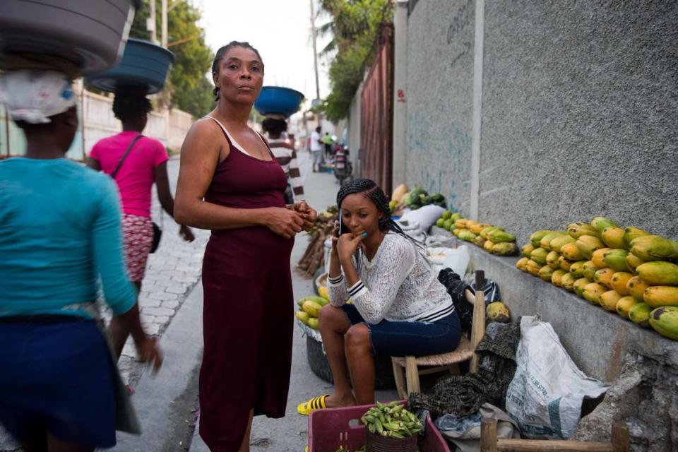 Wadlande Pierre, right, talks on her mobile phone as she helps her mother, Vanlancia Julien, center, at their fruit and vegetable stand on a sidewalk in Delmas, a district of Port-au-Prince, Haiti, on Nov. 27, 2019. Pierre, 23, said she temporarily moved in with her aunt in the southwest town of Les Cayes to escape the violent protests in Port-au-Prince.