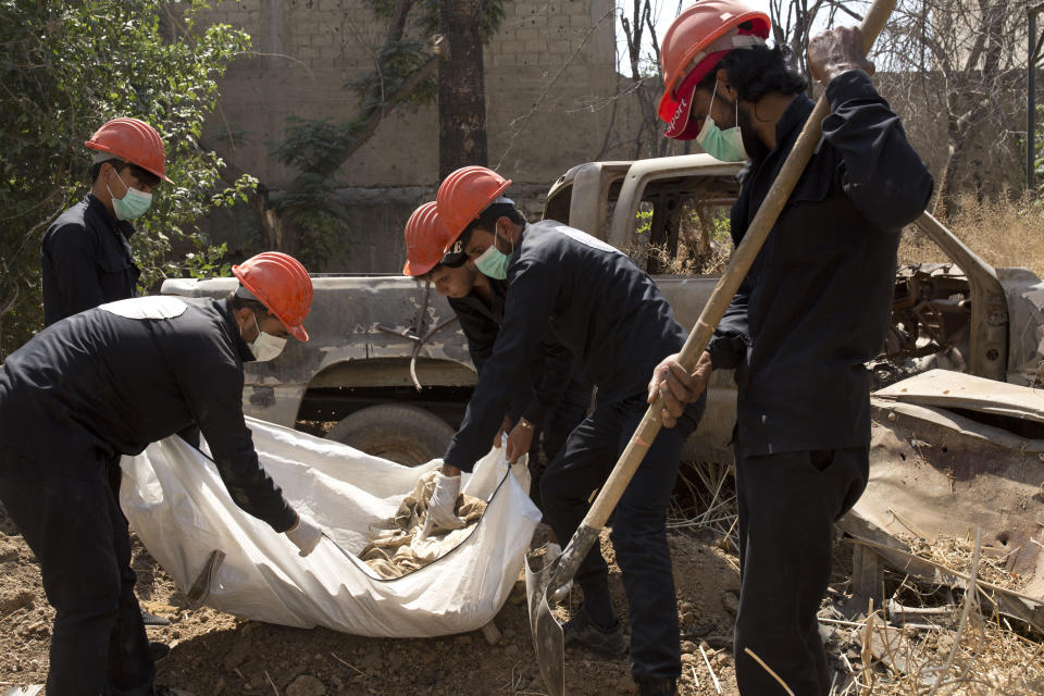 In this Saturday, Sept. 7, 2019 photo, first responders load human remains into a body bag at the site of a mass grave in Raqqa, Syria. First responders said they have pulled nearly 20 bodies out of the latest mass grave uncovered in Raqqa, the Syrian city that was the de facto capital of the Islamic State group. It is the 16th mass grave in the city, and officials are struggling with a lack of resources needed to document and one day identify the thousands of dead who have been dug out. (AP Photo/Maya Alleruzzo)