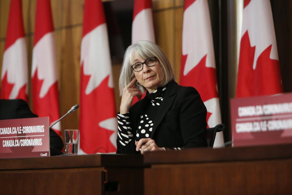 Patty Hajdu sits at a desk with Canadian flags behind her.