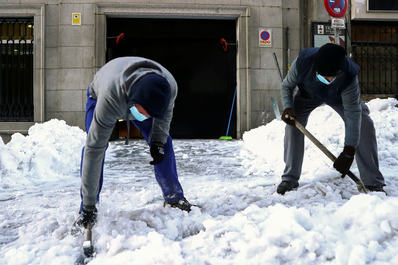 Workers use a hammer and a shovel to break ice, in Madrid