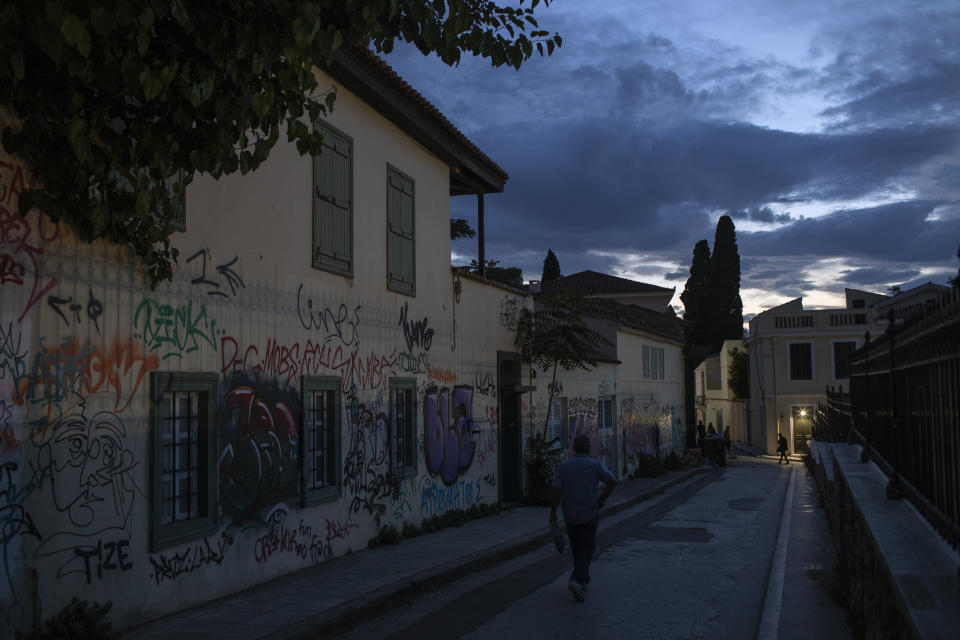 In this Wednesday, July 3, 2019 photo, a man walks next to graffiti covered houses in Plaka district, Athens. Lying under the shadow of the ancient Acropolis Hill, Plaka's narrow streets and neoclassical architecture have for decades attracted tourists and Athenians alike in central Athens.(AP Photo/Petros Giannakouris)