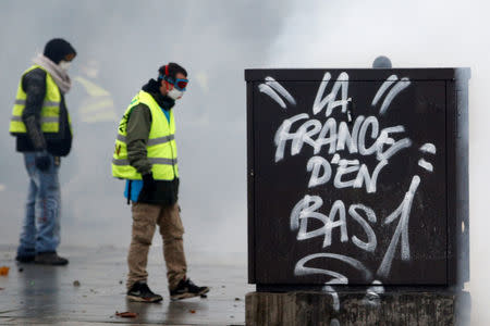 Protesters wearing yellow vests, a symbol of a French drivers' protest against higher diesel fuel taxes, walk among tear gas during clashes near the Place de l'Etoile in Paris, France, December 1, 2018. The slogan reads "The lower class of France". REUTERS/Stephane Mahe