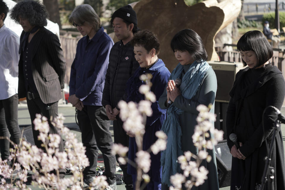 Artists and staff members at the stage stand to mourn for the victims of the 2011 earthquake and tsunami during an online special memorial event at Hibiya Park in Tokyo Thursday, March 11, 2021. Japan on Thursday marked the 10th anniversary of the massive earthquake, tsunami and nuclear disaster that struck Japan's northeastern coast. (AP Photo/Eugene Hoshiko)