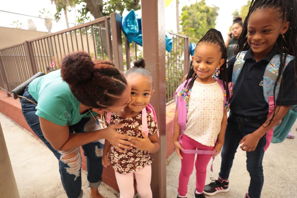 A mother kisses her two young daughters goodbye at school.