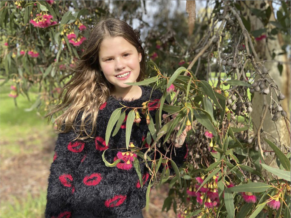 En esta image, tomada el 30 de abril de 2020 y proporcionada por su familia, Niki Jolene Berghamre-Davis, de 11 años, posa junto a un árbol en flor en Port Melbourne, Australia. “Después de esta pandemia de corona, cuando esto termine, creo que todo estará mucho más lleno de vida”, dice. (Anna Berghamre via AP)