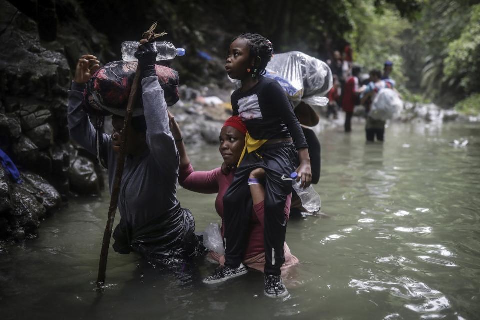 A child is hoisted onto an adult's shoulders as a woman and man wade through water.