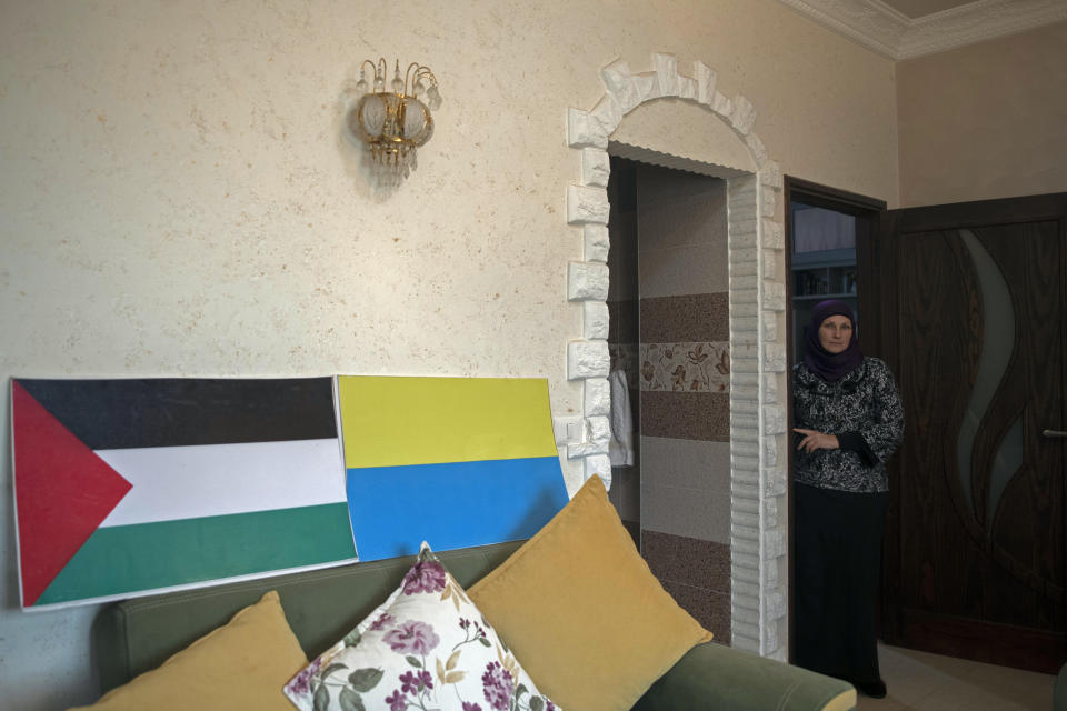 Ukrainian Oksana al-Astal poses for a photograph while standing in the living room of her home decorated with representations of the Palestinian and Ukrainian flags in Khan Younis, southern Gaza Strip, Sunday, March 13, 2022. The al-Astal family is among dozens of Palestinian-Ukrainian families in the isolated territory who have experienced several wars firsthand — the most recent last May — and are now watching another unfold in Ukraine, where many of them have loved ones. (AP Photo/ Khalil Hamra)