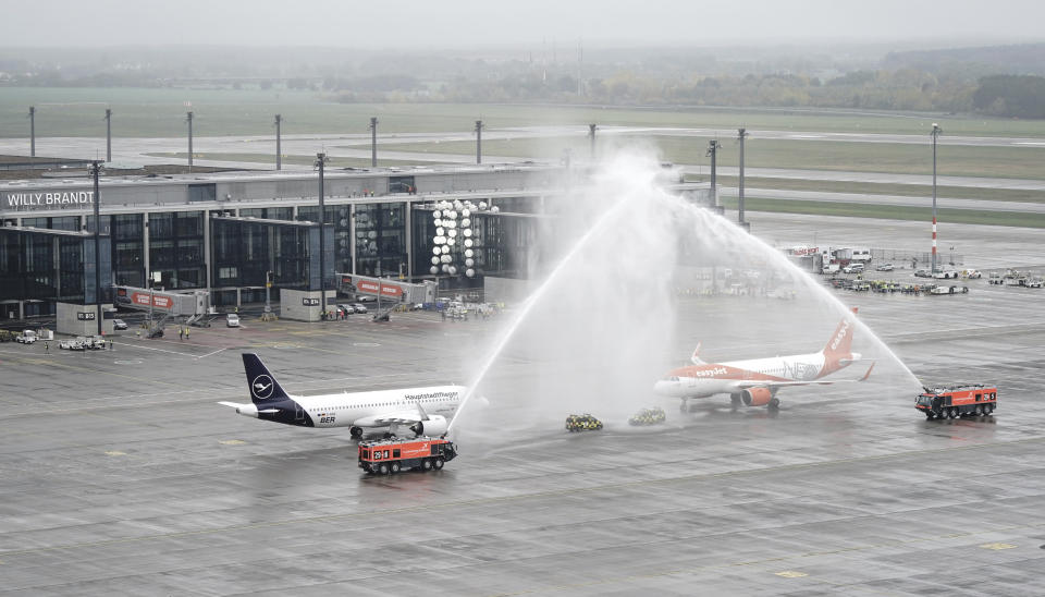 Planes of the airlines Lufthansa and Easyjet stand under a fountain from the airport's fire brigade in front of Terminal 1, to celebrate the opening of the new airport Berlin Brandenburg 'Willy Brandt', BER, in Schoenefeld near Berlin, Germany, Saturday, Oct. 31. The airport will open on 31.10.2020 after a long delay. (Kay Nietfeld/POOL via AP)