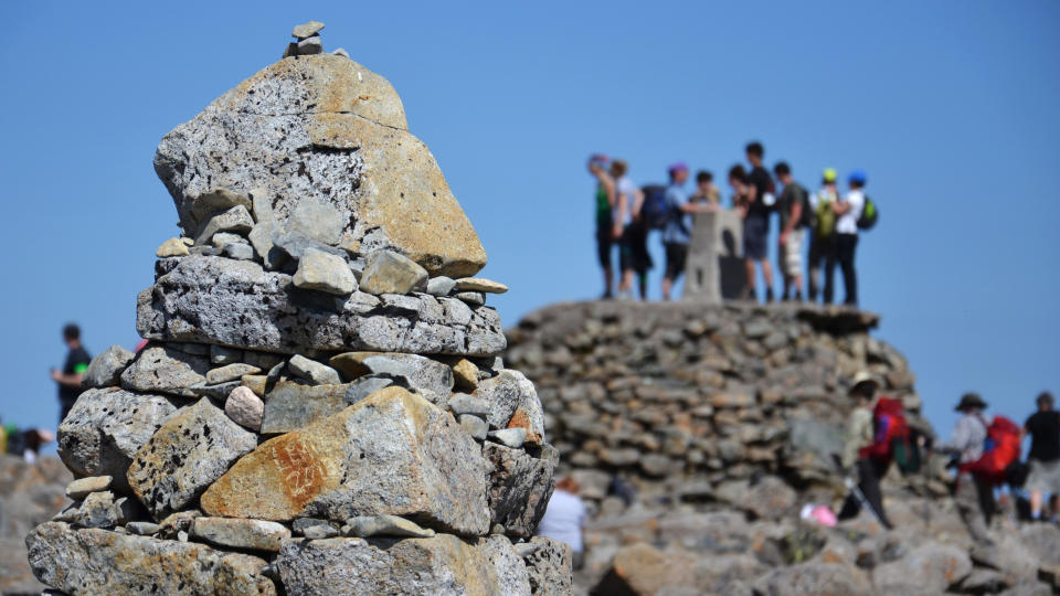 Rock cairn at the summit of Ben Nevis with hikers in the distance