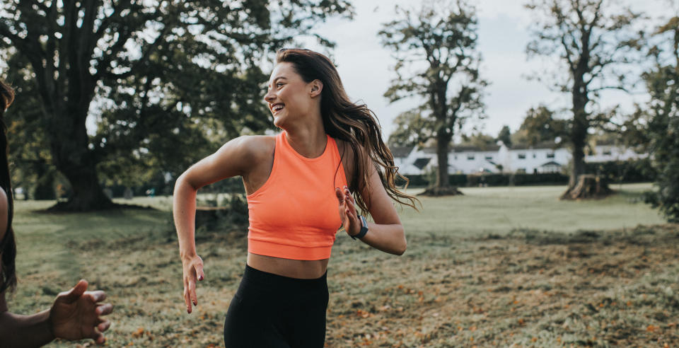 Single woman jogging through a park in the morning. She glances over her shoulder and laughs. Space for copy.