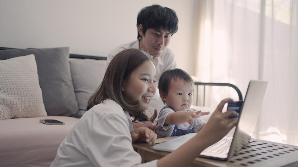 Man siting on couch looking at his wife shopping online and cute baby looking at laptop.