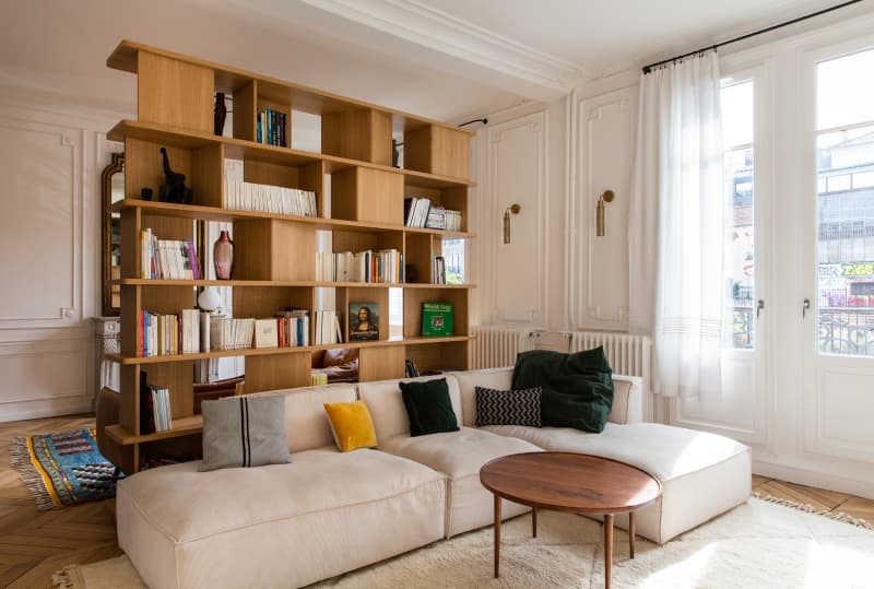 Cream colored sectional in living room with large wooden bookshelf.