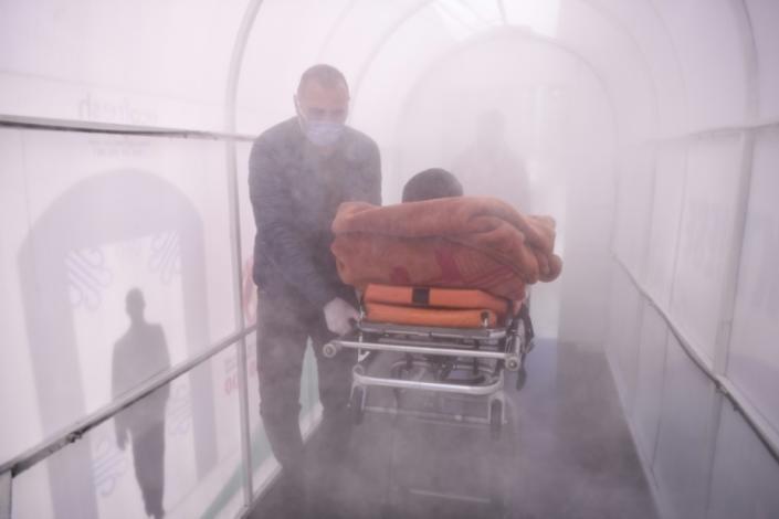 A health worker walks a patient through a disinfection chamber set up in front of a hospital in Mitrovica, Kosovo (AFP Photo/Armend NIMANI)