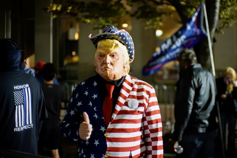 A supporter of U.S. President Donald Trump dressed with the U.S. flag colors and a mask depicting Trump gives a thumbs up as votes continue to be counted following the 2020 U.S. presidential election, in Philadelphia, Pennsylvania