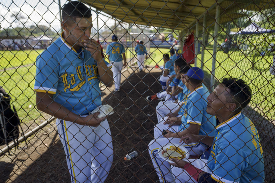 Nicaraguan Wilmer Ramos, sitting, shares corn tortillas with a teammate before they play in a preparation tournament before the start of the local baseball league at Sabana Park in San Jose, Costa Rica, Sunday, Aug. 28, 2022. The number of players for the local league in Costa Rica has increased since Nicaraguans began seeking asylum at the highest levels since their country['s political crisis exploded in April 2018. (AP Photo/Moises Castillo)