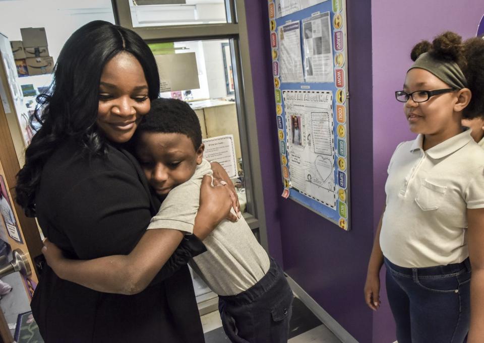 Teacher hugs a young student outside a classroom