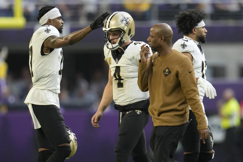 New Orleans Saints wide receiver A.T. Perry, left, pats the helmet of quarterback Derek Carr (4) as Carr walks off the field after being injured during the second half of an NFL football game against the Minnesota Vikings Sunday, Nov. 12, 2023, in Minneapolis. (AP Photo/Abbie Parr)