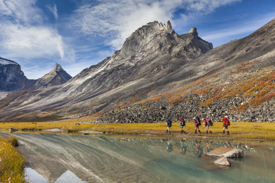 Group of hikers walking beside a mountain lake with towering peaks in the background