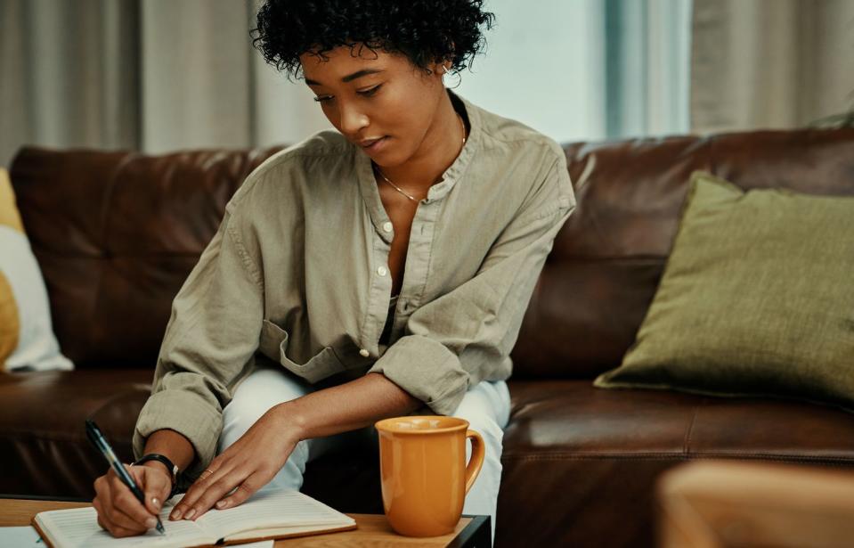 cropped shot of a beautiful young woman writing in her notebook while sitting at home