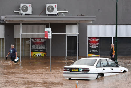 Local residents walk past a damaged car as floodwaters enter the main street of the northern New South Wales town of Lismore, Australia, March 31, 2017 after heavy rains associated with Cyclone Debbie swelled rivers to record heights across the region. AAP/Dave Hunt/via REUTERS