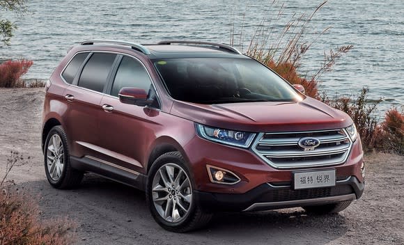 A red Ford Edge, a midsize crossover SUV, parked on a waterfront. The Edge has a Chinese-language front license plate.