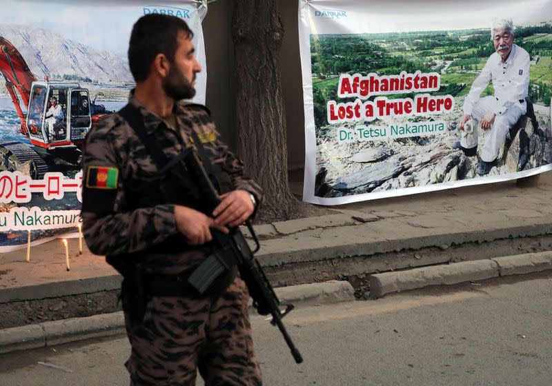 An Afghan security force stands guard in front of a poster depicting Japanese doctor Tetsu Nakamura, who was killed in Jalalabad in yesterday's attack, in Kabul