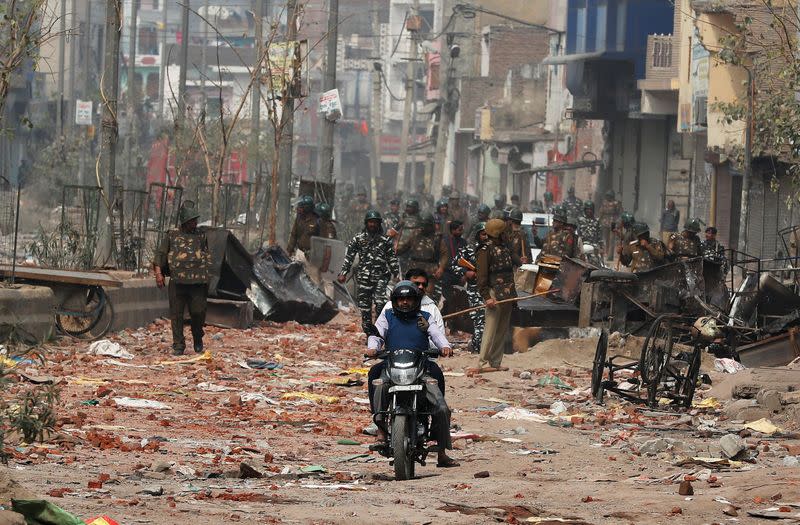 Men ride a motorcycle past security forces patrolling a street in a riot affected area after clashes erupted between people demonstrating for and against a new citizenship law in New Delhi