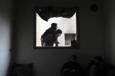 Abu Nejme, a 21-year-old Free Syrian Army fighter, is carried by a fellow fighter as seen through a window in Aleppo January 10, 2015. REUTERS/Jalal Al-Mamo