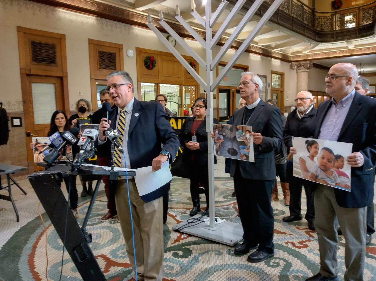 Darryl Morin, National President of Forward Latino, speaks during a press conference at City Hall Tuesday, Dec. 20, decrying Title 42, a Trump-era immigration policy that has prevented thousands of migrants from seeking asylum in the US. He is flanked by supporters holding pictures of migrants taken during a tour of refugee camps along the Mexico and US border.