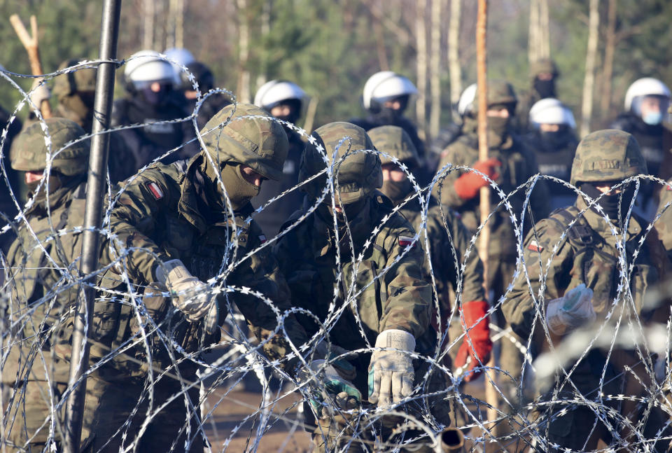 Polish police and border guards stand attach the barbed wire as migrants from the Middle East and elsewhere gather at the Belarus-Poland border near Grodno Grodno, Belarus, Tuesday, Nov. 9, 2021. Hundreds if not thousands of migrants sought to storm the border from Belarus into Poland on Monday, cutting razor wire fences and using branches to try and climb over them. The siege escalated a crisis along the European Union's eastern border that has been simmering for months. (Leonid Shcheglov/BelTA via AP)