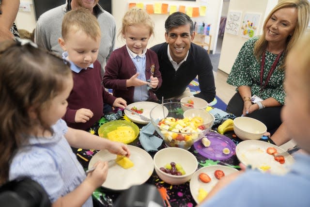 Rishi Sunak smiles while watching three school children prepare fruit