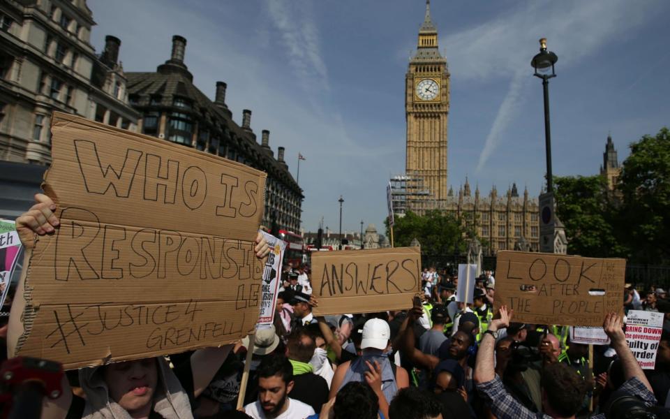 Protesters hold up placards about the Grenfell Tower tragedy as they gather in Parliament Square after marching through central London - AFP