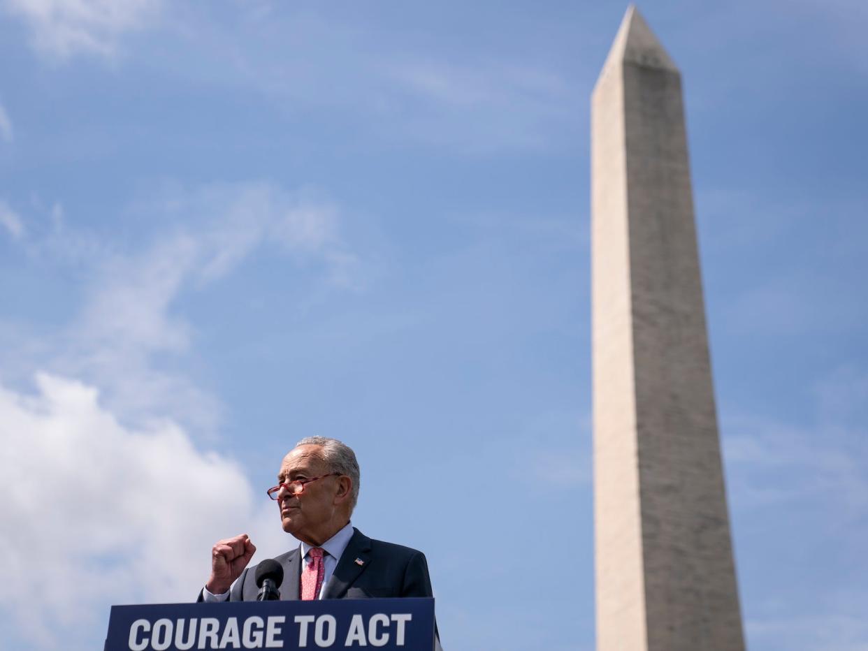 Senate Majority Leader Chuck Schumer, standing at a lectern bearing a sign that reads "Courage to Act," addresses reporters during an outdoor press conference held beside the Washington National Monument.