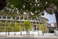 Cherry blossom flowers bloom outside the Japan National Stadium, where opening and closing ceremonies and other events for the Tokyo 2020 Olympics will be held, as a guard closes the gate along the fence Tuesday, April 6, 2021, in Tokyo. Tokyo pitched itself as "a safe pair of hands” when it was awarded the Olympics 7 1/2 years ago. Now, nothing is certain as Tokyo's postponed Olympics hit the 100-days-to-go mark on Wednesday, April 14, 2021. (AP Photo/Kiichiro Sato)