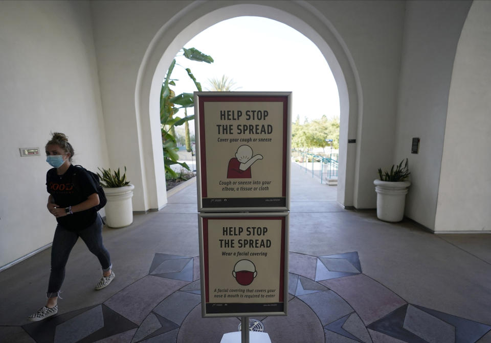 FILE - In this Sept. 2, 2020, file photo, a woman wears a mask as she walks on campus at San Diego State University in San Diego. A coronavirus outbreak of more than 700 cases reported at San Diego State University has put all of San Diego County, with more than 3 million people, at risk of having to close indoor dining and shopping, many for a third time under California guidelines. (AP Photo/Gregory Bull, File)