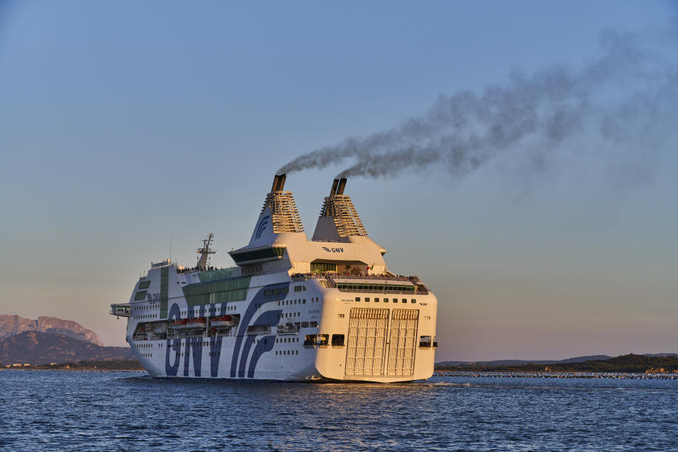 A large cruise ship with the name "GNV" is sailing through calm waters during what appears to be either sunrise or sunset, with mountains visible in the background