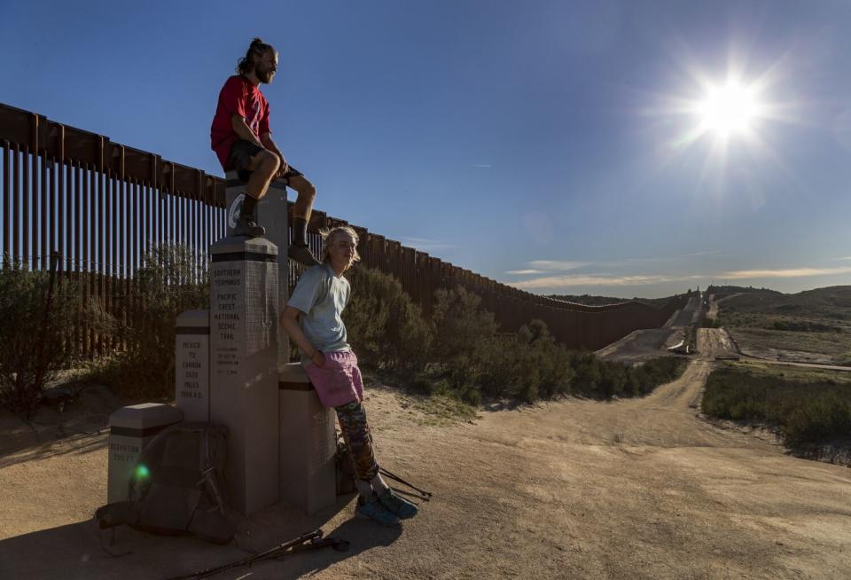 One hiker sits while the other stands beneath him along a dirt path