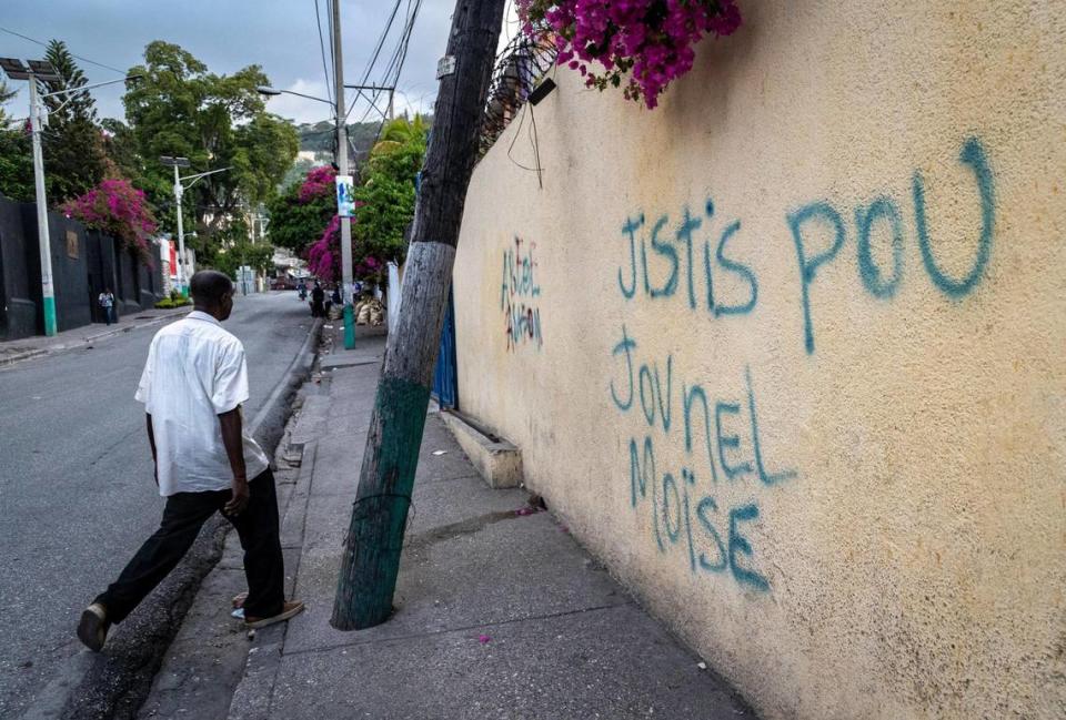 A man walks by graffiti on a wall demanding justice for slain Haitian President Jovenel Moïse in Pétionville. Normally the street would fhave been be clogged with bumper-to-bumper traffic. But fear has many people staying off the streets or going home early.