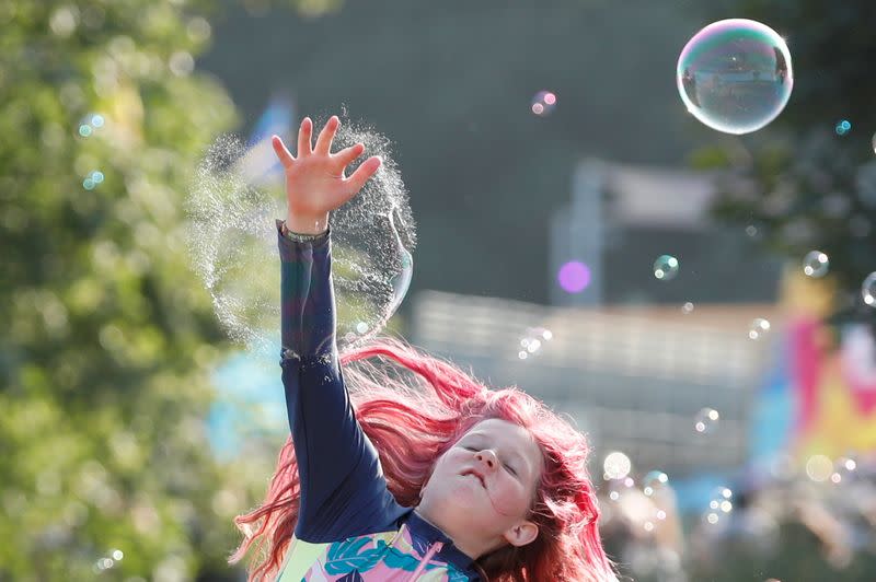 A young festivalgoer jumps to burst a bubble at Latitude Festival at Henham Park