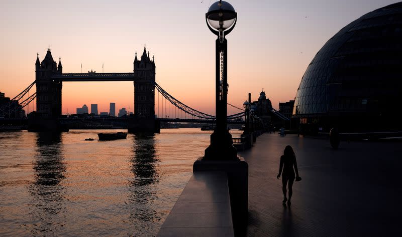FILE PHOTO: A woman walks near City Hall and Tower Bridge at dawn in London