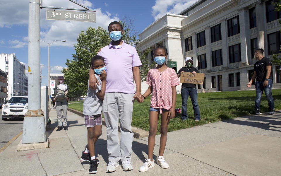 Jerry-Pale Molcolo with his children, Moetapele Green, 9, left, and Amirial Green, 12 watch protesters confront the police on Campbell Avenue downtown Roanoke on Saturday, May 30, 2020. Following a rally at Washington Park organized by the local Black Lives Matter chapter, demonstrators marched toward the police station on Campbell Avenue and were met by multiple police barricades.(Heather Rousseau/The Roanoke Times via AP)