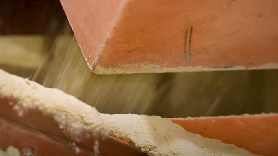Closeup of red machinery outputting ground sawdust-like material.