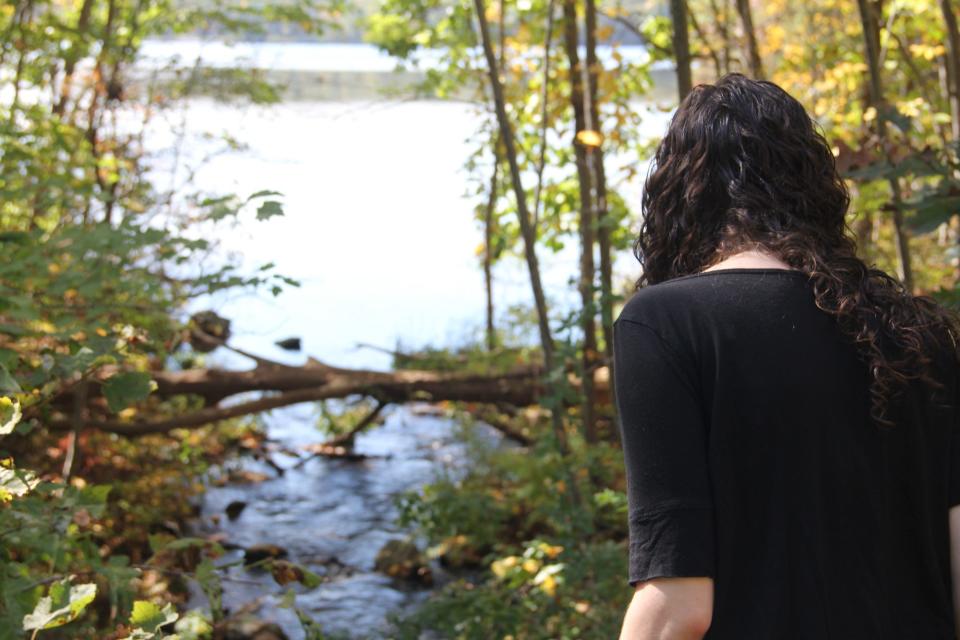 A woman looking out into a wooded brook.