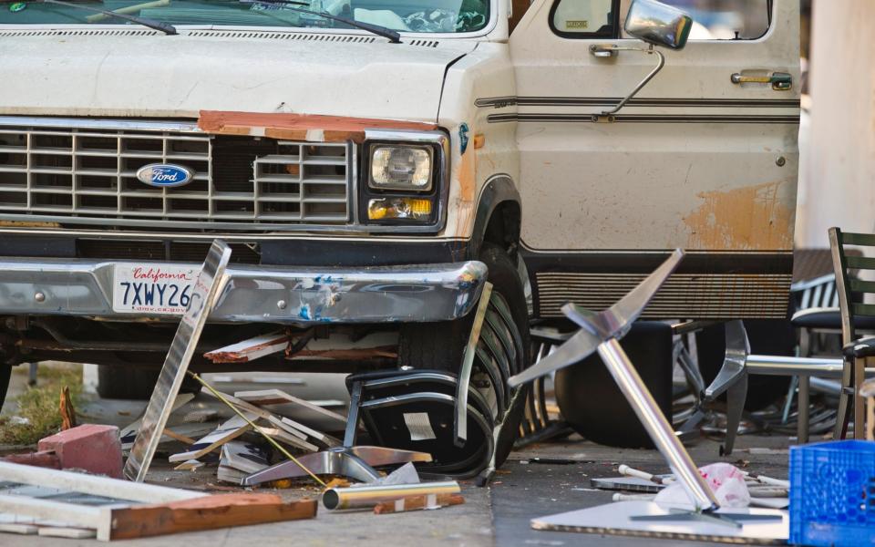 Broken restaurant tables and chairs are seen under a van that plowed into a group of people dining on a Los Angeles pavement - Credit: AP