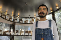 Corey Cantu looks out from the cookie kiosk he works at Friday, Oct. 18, 2019, in San Francisco. California's jobless rate has fallen to a record low 4% and in San Francisco it's dropped under 2%, a level economists once thought impossible to reach. In that city, the building cranes that dot the skyline are emblematic of a booming economy but the sidewalks filled with homeless and workers struggling to find affordable housing tell a different story. Cantu, who tends an artisanal cookie kiosk in downtown San Francisco, said that on top of his full-time job, he also walks dogs and does stick-and-poke tattoos and sells his paintings to make ends meet. (AP Photo/Olga Rodriguez)