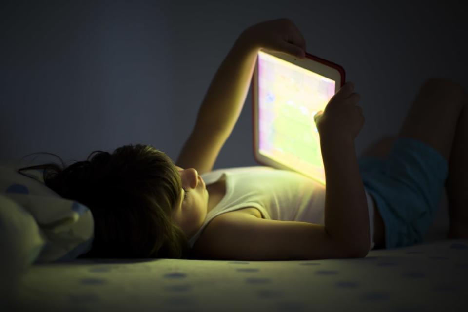 A child lying on a bed staring at an iPad