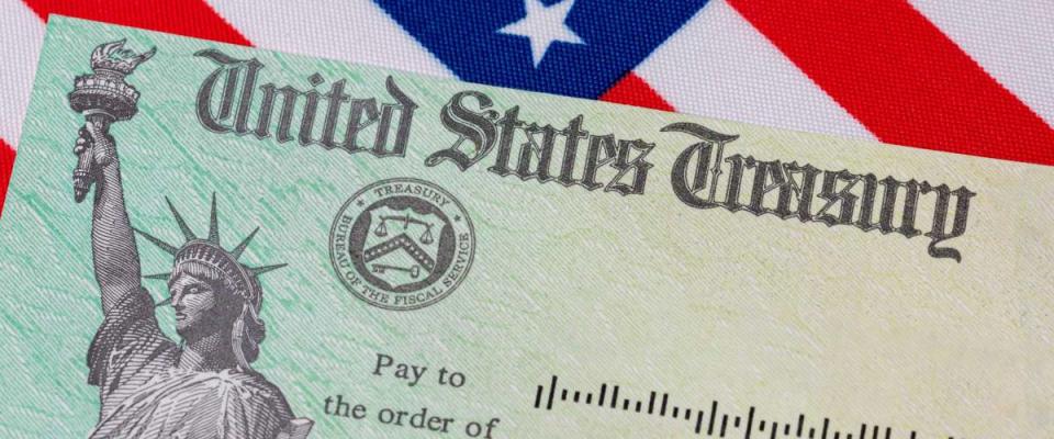 United States Treasury check and American flag. Concept of stimulus payment, tax refund and federal government grants, loans, benefits and assistance